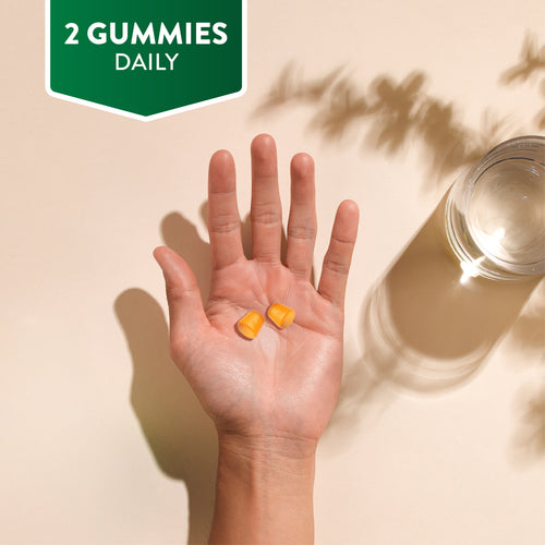 Two orange gummies are held in a hand. A green banner in the corner reads '2 GUMMIES DAILY'.