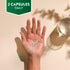 A hand holds two translucent capsules, text reads '2 CAPSULES DAILY', with a glass of water also visible.