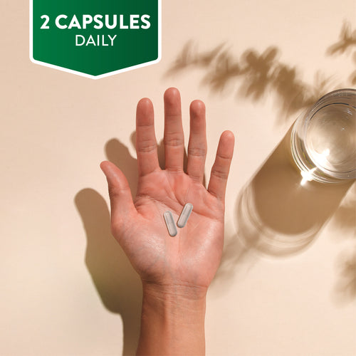 A hand holds two translucent capsules, text reads '2 CAPSULES DAILY', with a glass of water also visible.