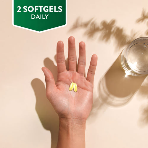 A hand holds two yellow Pumpkin Seed Oil softgels. A corner graphic reads '2 SOFTGELS DAILY'.